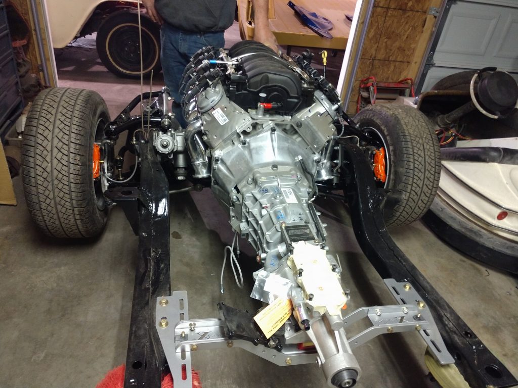 Car chassis with engine and transmission installed, in a garage setting. - Monarch Showroom