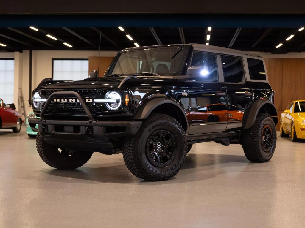 A black ford bronco parked indoors with other vehicles in the background. - Monarch Showroom