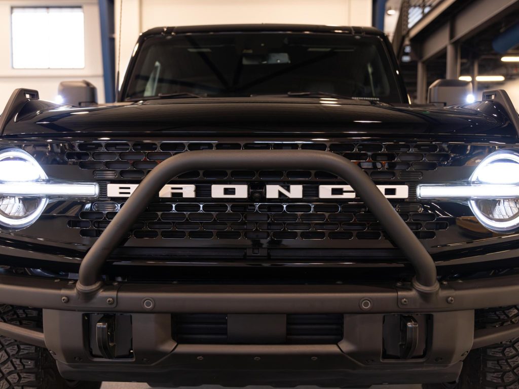 Front view of a ford bronco vehicle with illuminated headlights and a prominent grille. - Monarch Showroom