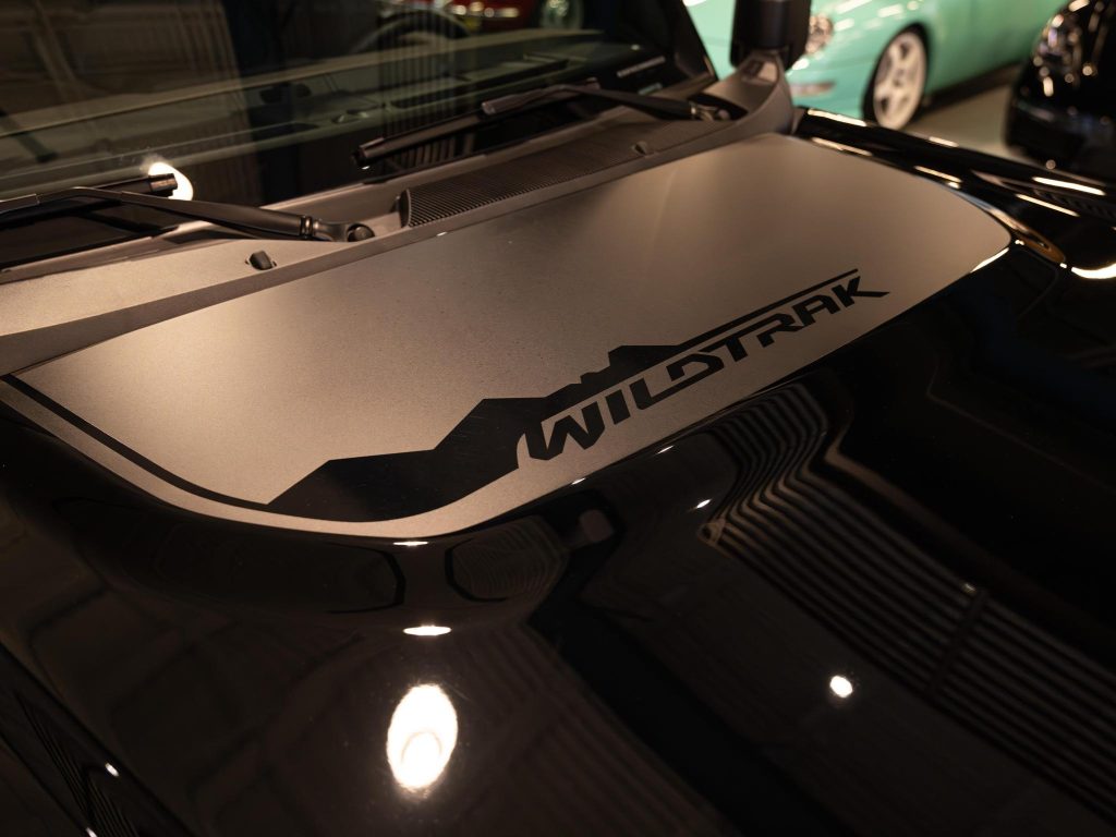 Close-up of a vehicle's hood with the "wildtrak" decal, possibly indicating a ford ranger model, with another car reflected in the background. - Monarch Showroom