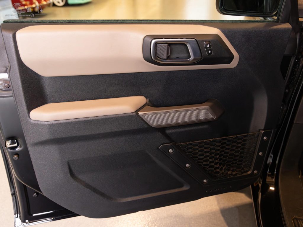 Interior door panel of a modern vehicle with control buttons, armrest, and speaker grille. - Monarch Showroom