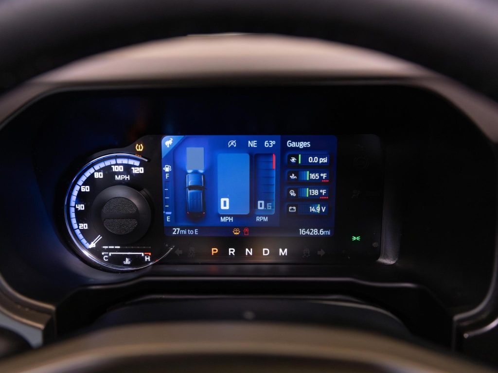 Digital dashboard display of a vehicle showing speedometer, gear position, and engine gauges. - Monarch Showroom