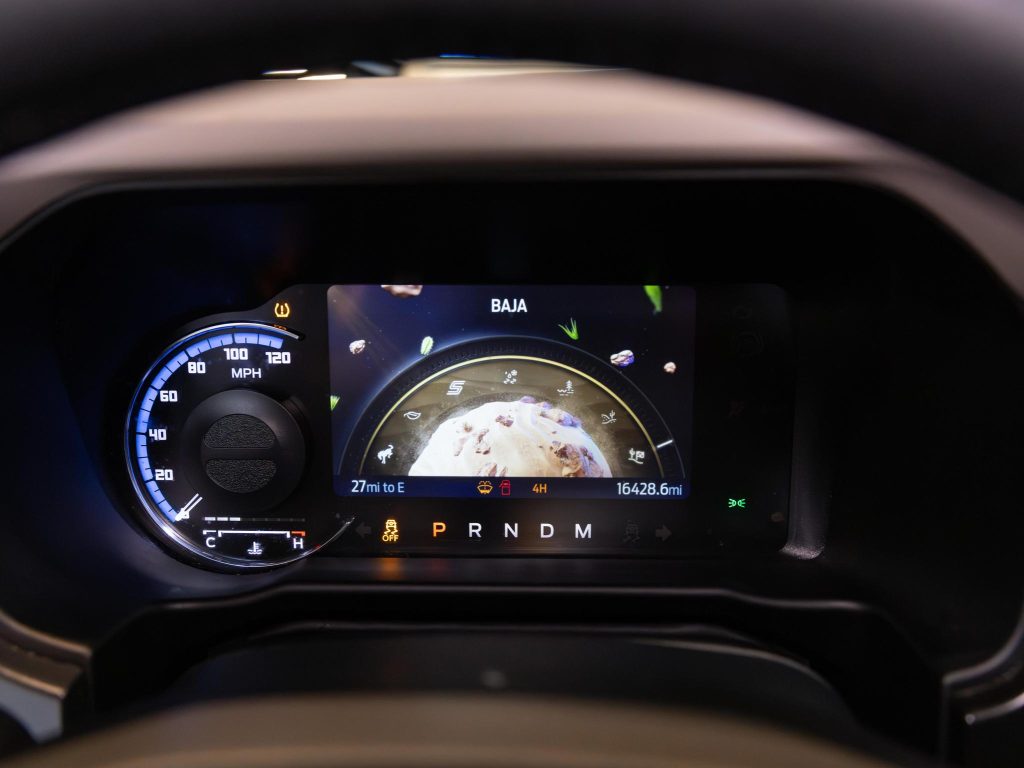 Digital car dashboard displaying speedometer, gear selection, driving mode 'baja', and a central screen with off-road terrain graphic. - Monarch Showroom