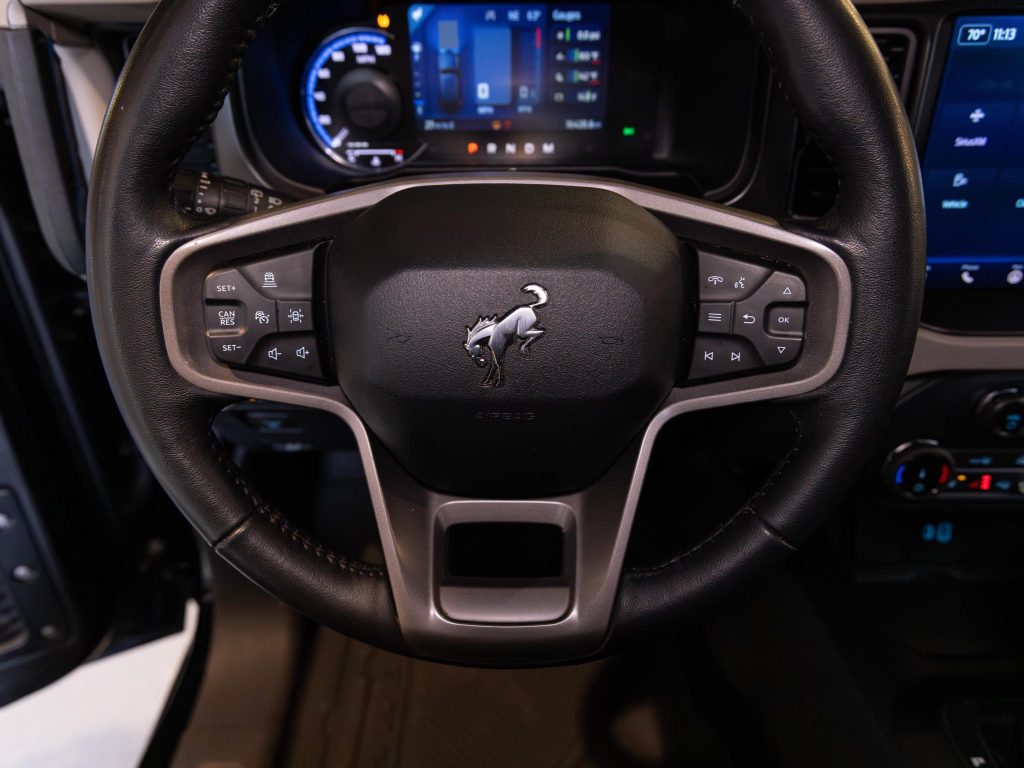Close-up view of a modern car's steering wheel with mounted controls and a logo in the center. - Monarch Showroom