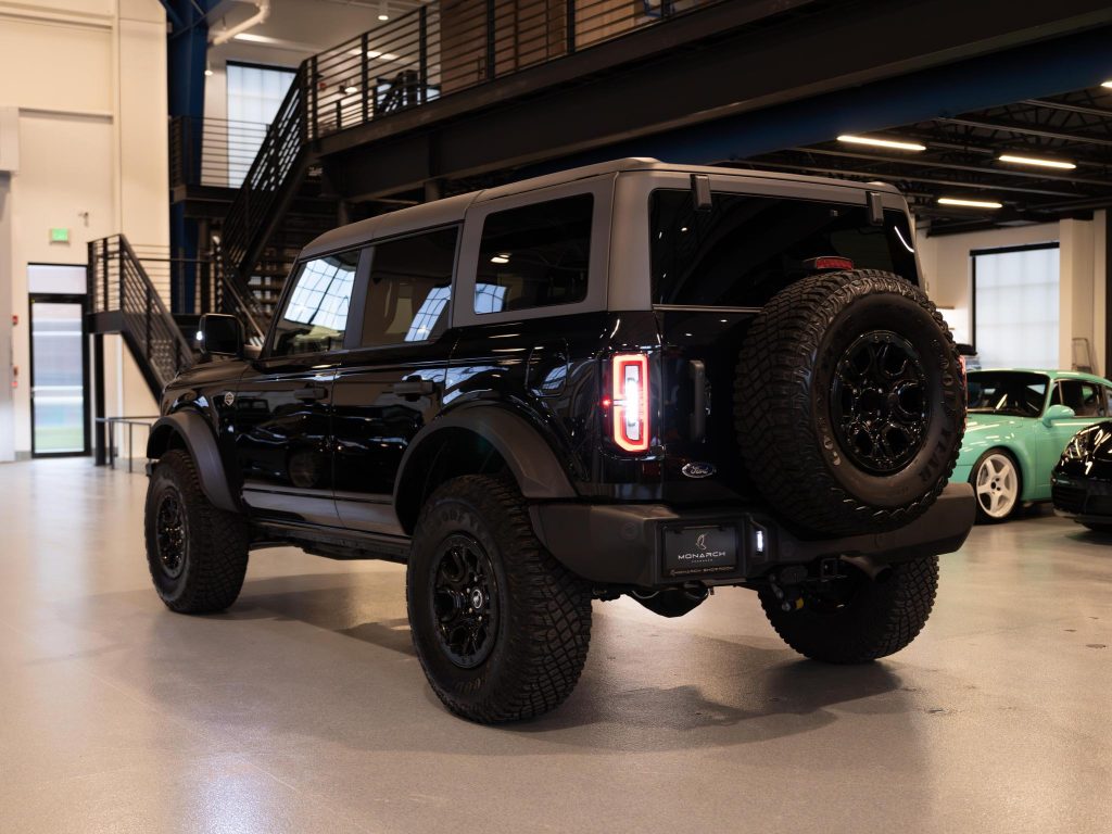 Black off-road vehicle with a spare tire mounted on the back, parked indoors. - Monarch Showroom