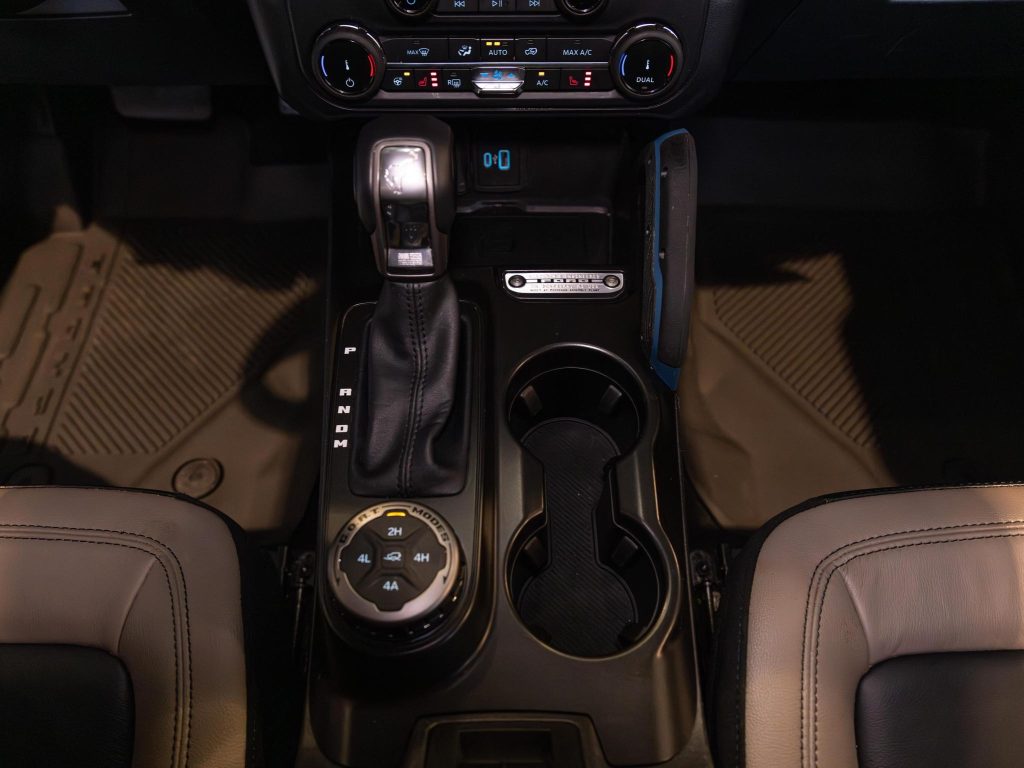 Interior view of a vehicle's center console featuring an automatic gear shifter, 4-wheel drive selector, and cup holders. - Monarch Showroom