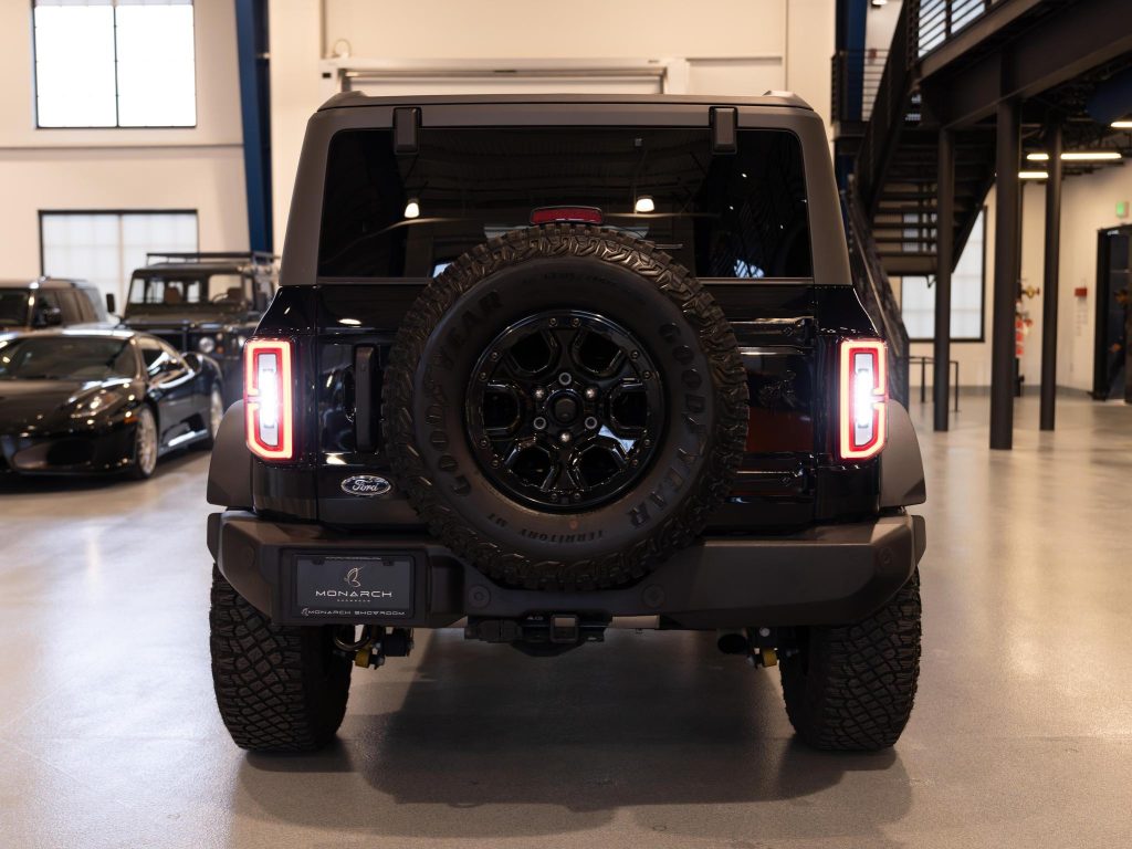 Rear view of a black ford bronco with a spare tire mounted on the tailgate in a showroom. - Monarch Showroom