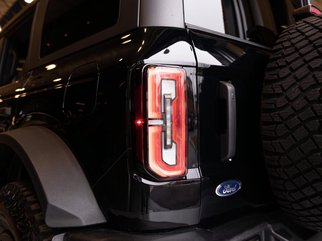 Close-up of a lit tail light on a black ford vehicle with a spare tire mounted on the back. - Monarch Showroom