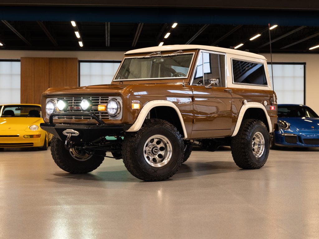 Vintage brown suv showcased in a showroom with classic and sports cars in the background. - Monarch Showroom