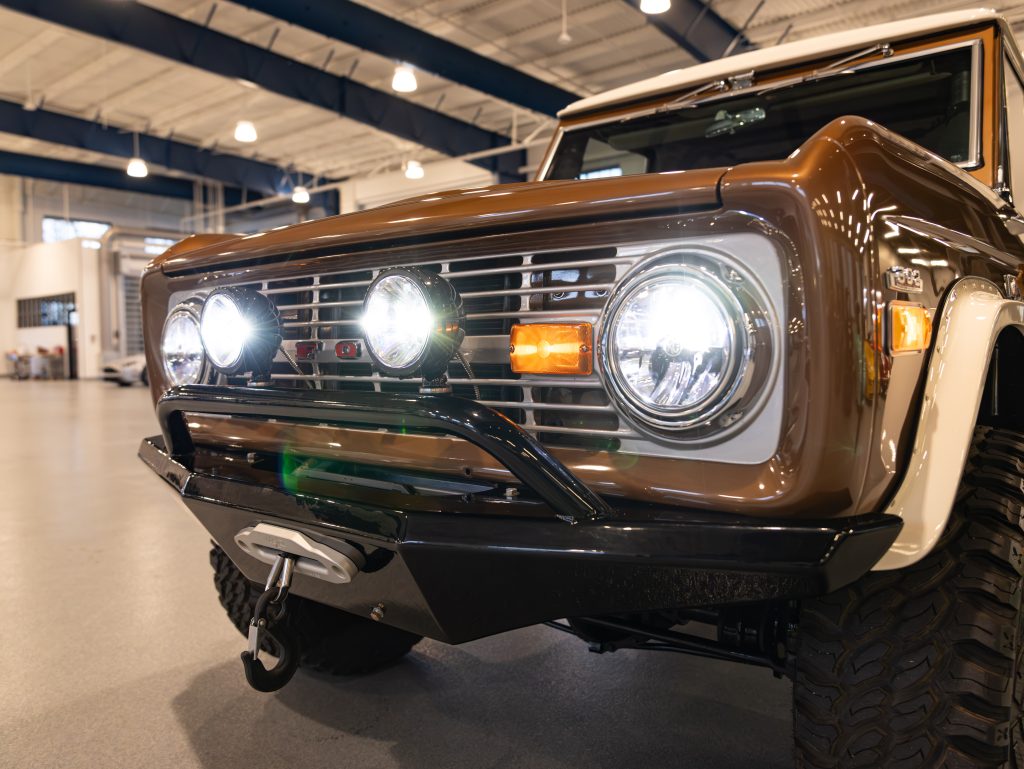 Close-up of a vintage brown suv with round headlights and a chrome bumper, displayed in a showroom. - Monarch Showroom