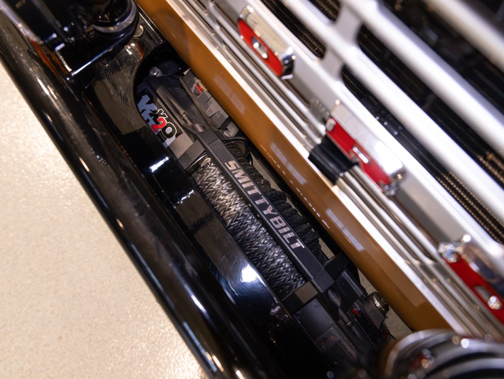 Close-up of a smittybilt vehicle winch mounted on a vehicle, with visible metallic parts and branding. - Monarch Showroom