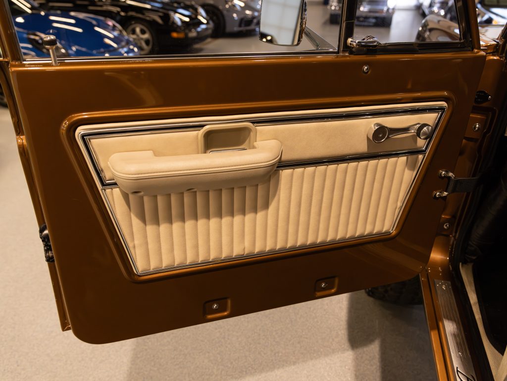 Interior door panel of a vintage car featuring brown and beige colors with a handle and pleated upholstery design. - Monarch Showroom