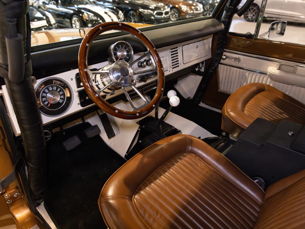Interior of a vintage car featuring a wooden steering wheel, classic dashboard, and brown leather seats. - Monarch Showroom
