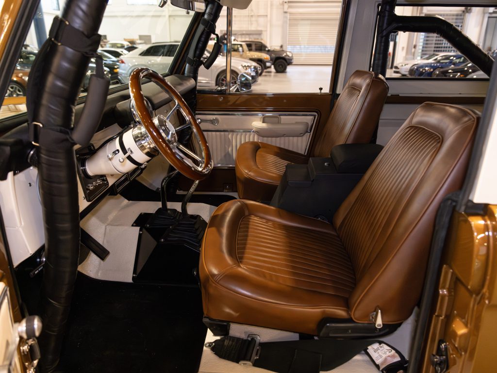 Interior view of a vintage car showing brown leather seats, a steering wheel, and a wooden dashboard. - Monarch Showroom