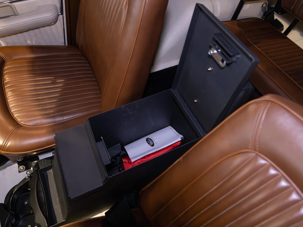Interior of a classic car showing an open center console with items inside, between two brown leather seats. - Monarch Showroom
