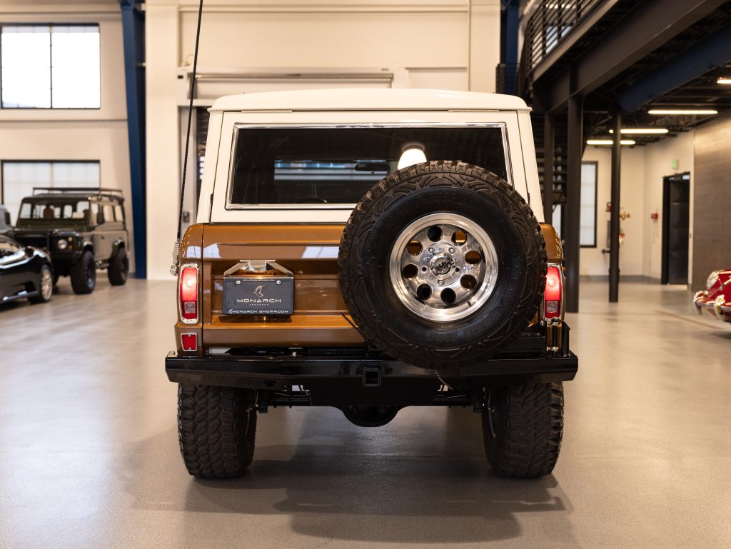 Rear view of a vintage brown and white suv with a spare tire mounted on the back, parked indoors. - Monarch Showroom