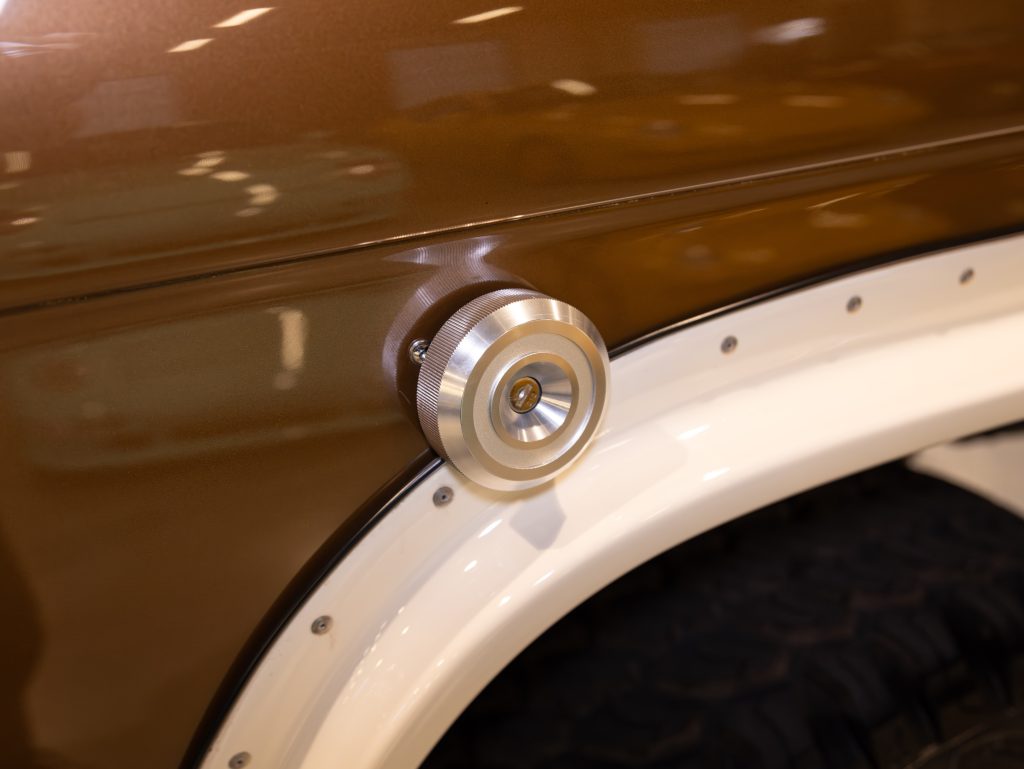 Close-up of a vehicle's fuel cap with a brushed metal finish on a brown car body with white fender trimming. - Monarch Showroom