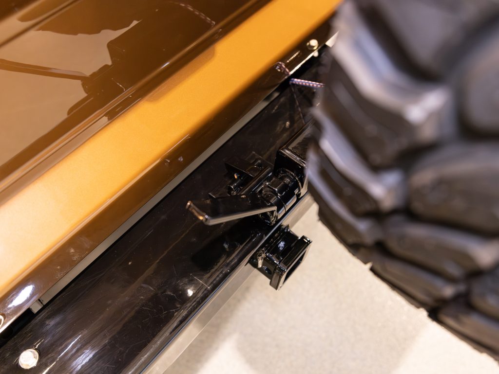 Close-up of a vehicle door hinge mechanism on a golden car with a black accent. - Monarch Showroom