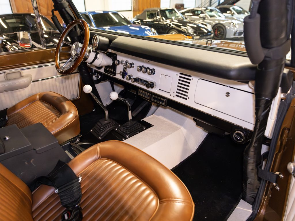 Interior view of a vintage car featuring brown leather seats, a manual transmission, and classic dashboard controls. - Monarch Showroom