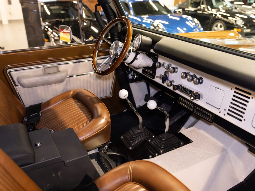 Interior view of a vintage car with brown leather seats, a manual transmission, and a classic dashboard design. - Monarch Showroom