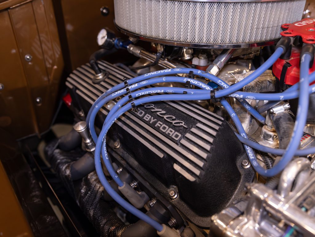 A detailed view of a shelby cobra engine with blue ignition wires and an air filter. - Monarch Showroom