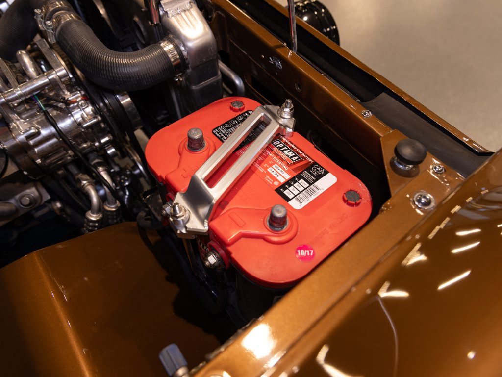 A close-up view of a red automotive battery installed in a vehicle engine bay. - Monarch Showroom