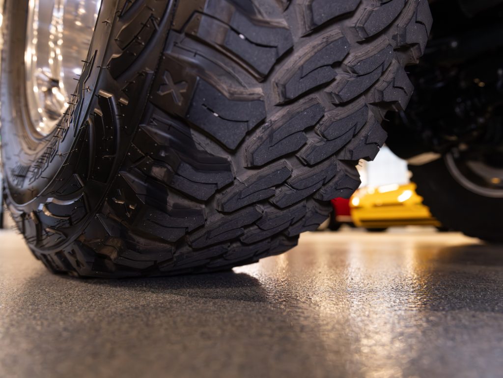 Close-up of a vehicle's tire tread pattern with a blurred car in the background. - Monarch Showroom