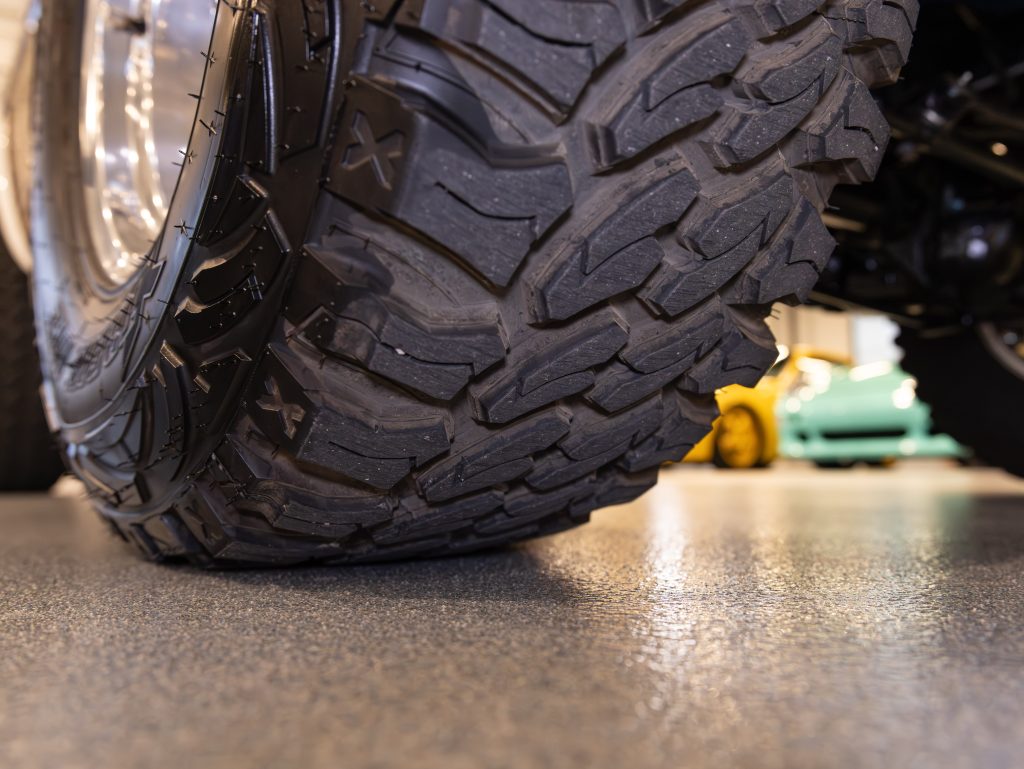 Close-up view of a motorcycle tire tread on a textured floor with vehicles in the background. - Monarch Showroom