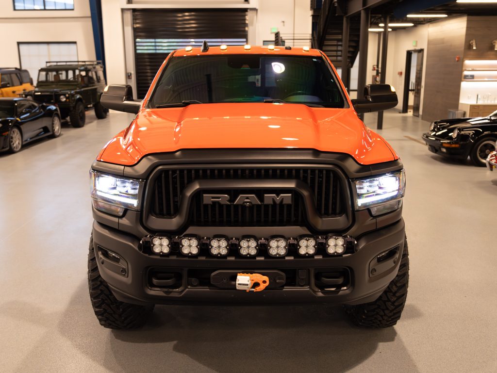 Orange ram truck on display indoors with additional lights mounted on the front grille. - Monarch Showroom