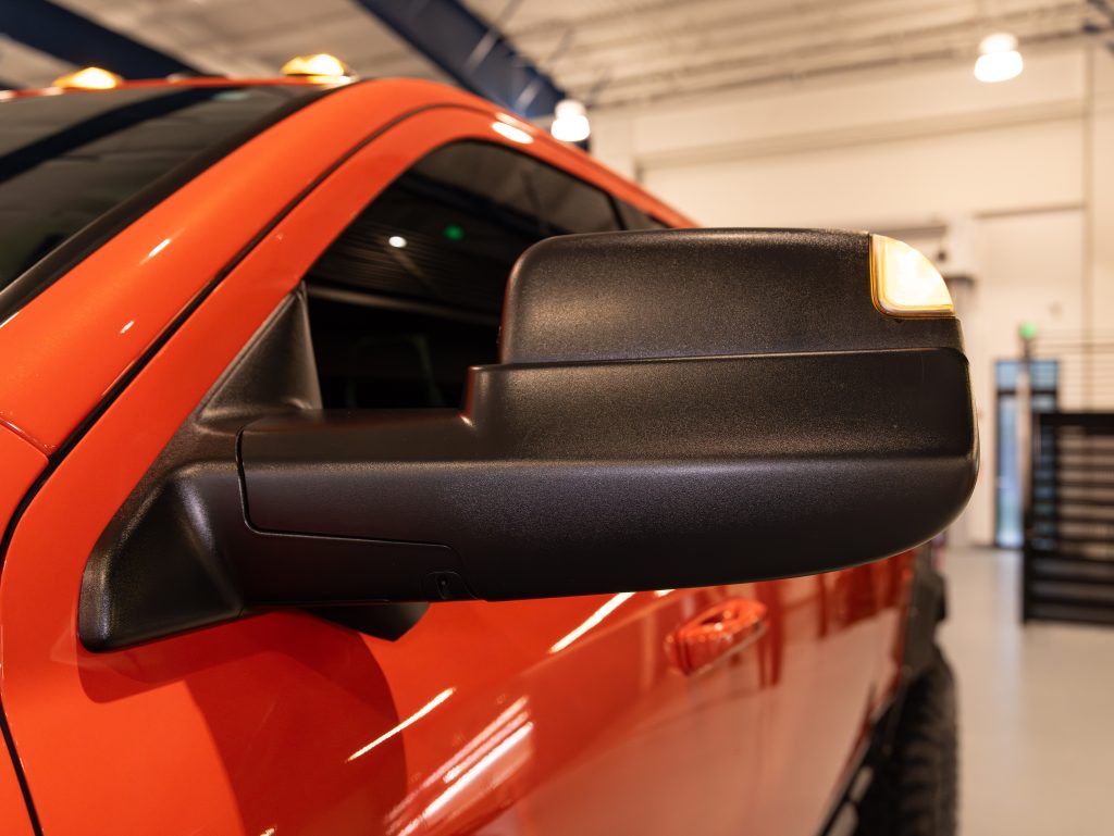Close-up of an orange vehicle's side mirror with integrated turn signal. - Monarch Showroom