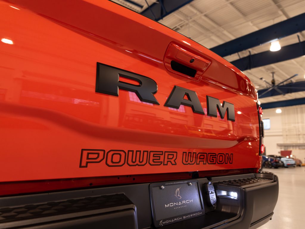 Close-up of a red ram power wagon truck tailgate with emblems, parked indoors. - Monarch Showroom