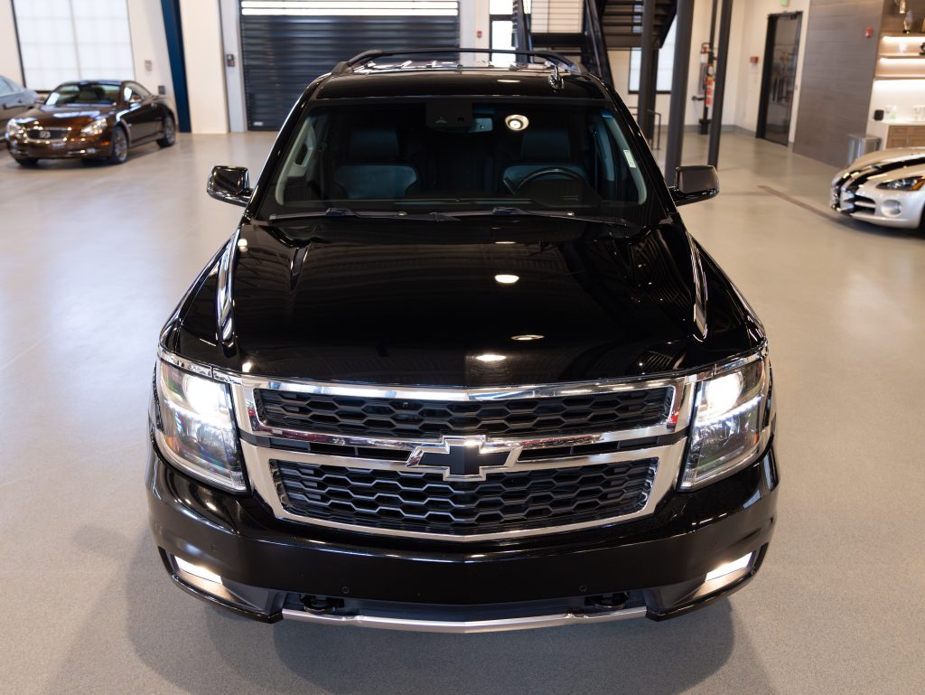 Black Chevrolet SUV parked indoors with a visible grille and headlights. Other vehicles are seen in the background, and a staircase is visible to the right. - Monarch Showroom