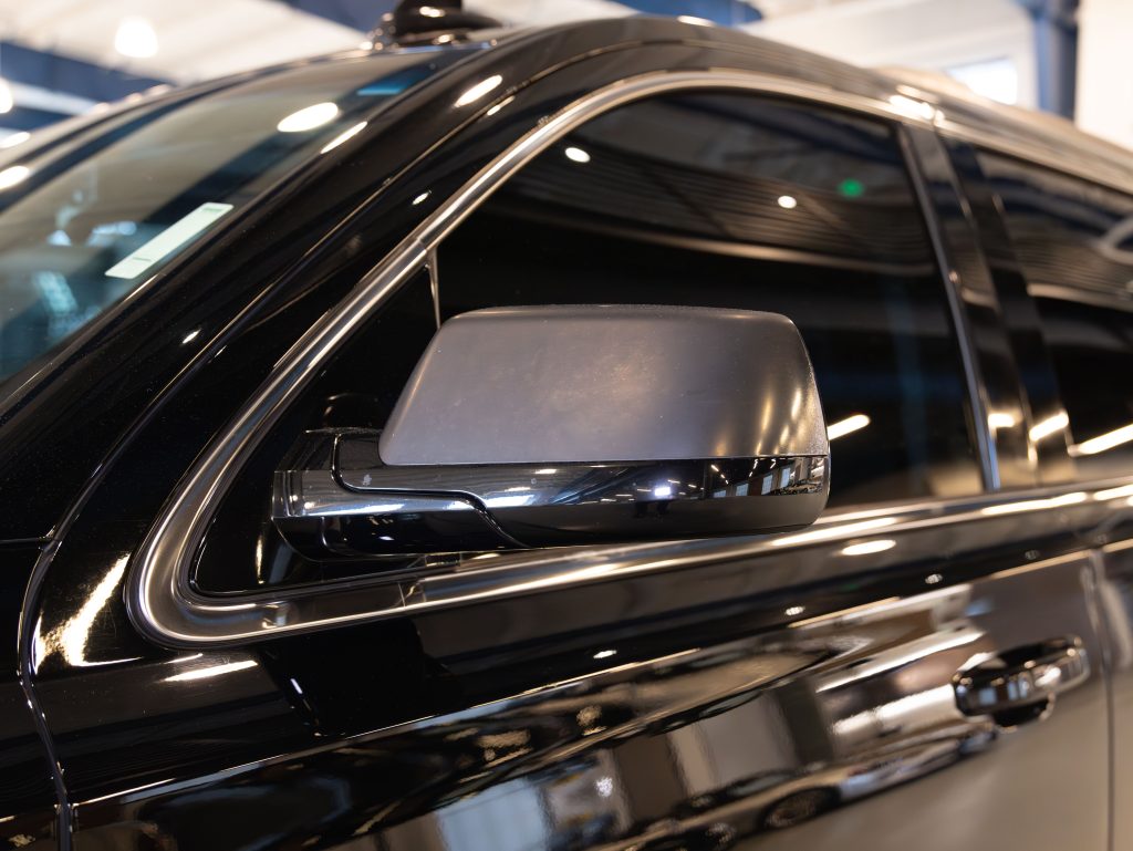 Side view of a black vehicle's door with a reflective side mirror, set in an indoor showroom with overhead lighting. - Monarch Showroom