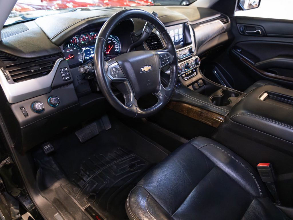 Interior of a vehicle showcasing a black leather steering wheel with a Chevrolet logo, dashboard gauges, and control panel. Black leather seats and cup holders are visible. - Monarch Showroom