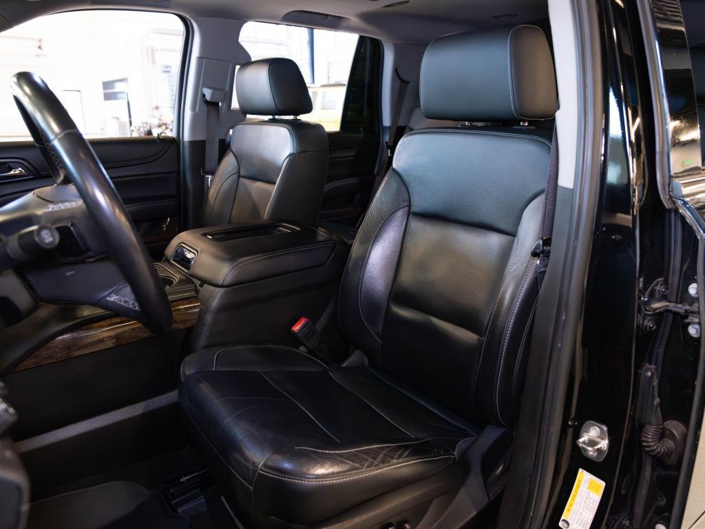 Interior of a vehicle showing black leather front seats, steering wheel, and dashboard, with a center console between the seats. - Monarch Showroom