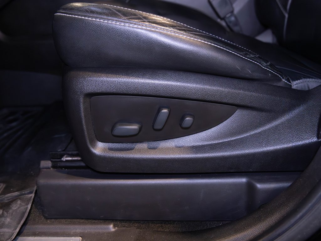 Close-up of a car seat with black leather upholstery, showing electronic adjustment controls on the side. - Monarch Showroom