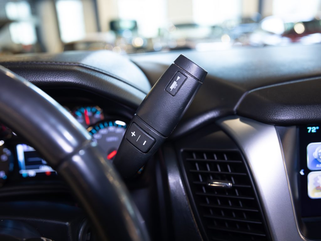 Close-up of a car's interior showing the gear shift lever on the steering column with plus and minus buttons, dashboard with speedometer, and partial view of infotainment screen displaying temperature. - Monarch Showroom