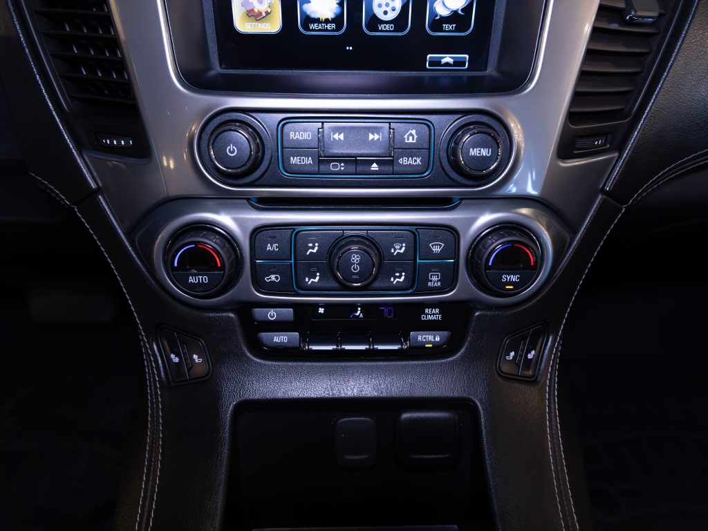 Close-up of a car dashboard console featuring a digital display, radio buttons, climate control dials, and other vehicle control buttons. - Monarch Showroom