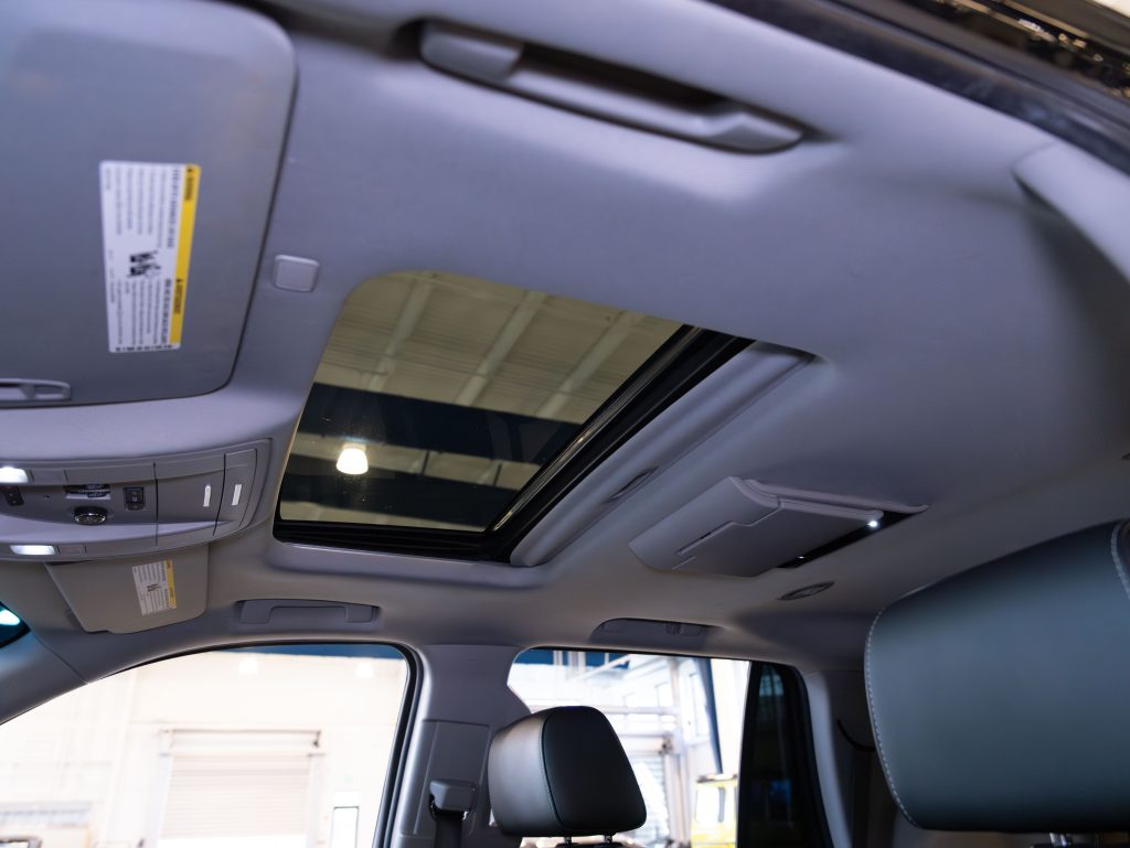 Car interior showing an open sunroof, a rearview mirror, overhead console with buttons, and a partial view of the driver’s seat and headrest. - Monarch Showroom