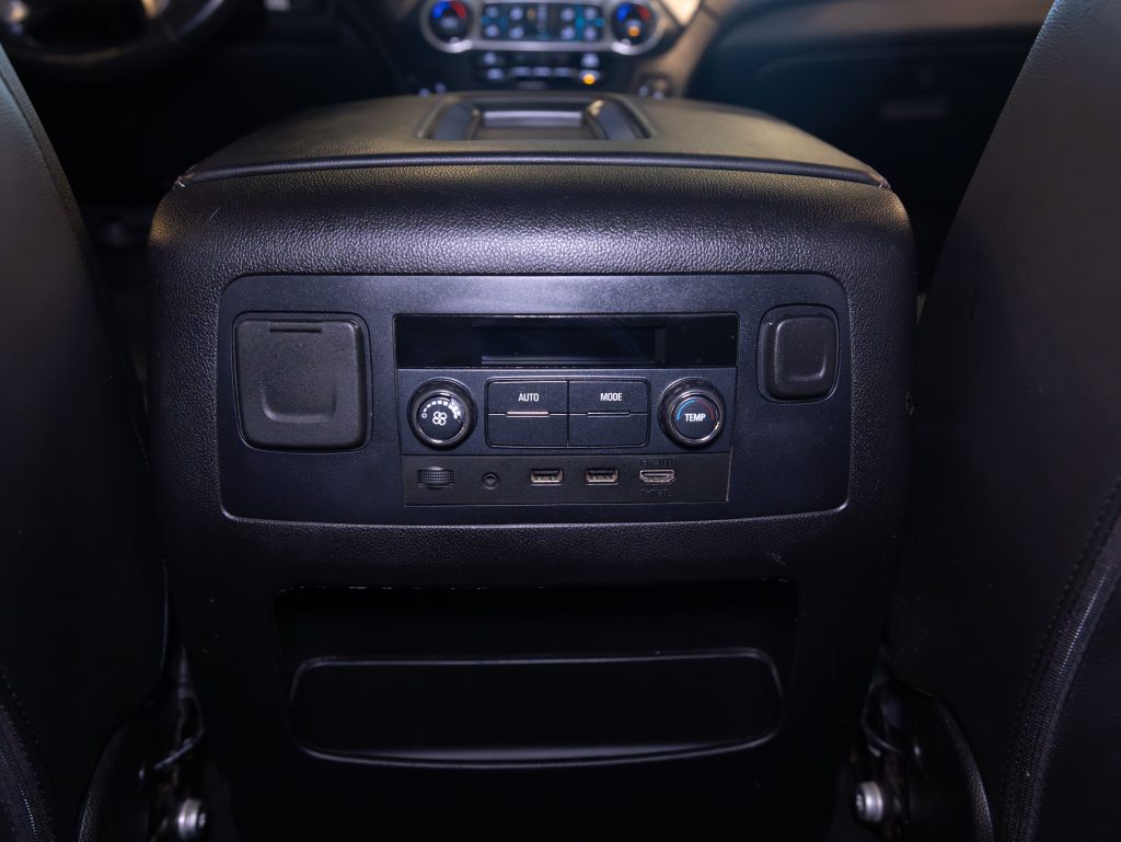 Rear vehicle console with climate controls, two USB ports, a 12V socket, and mode adjustment knob, set against black leather seats. - Monarch Showroom