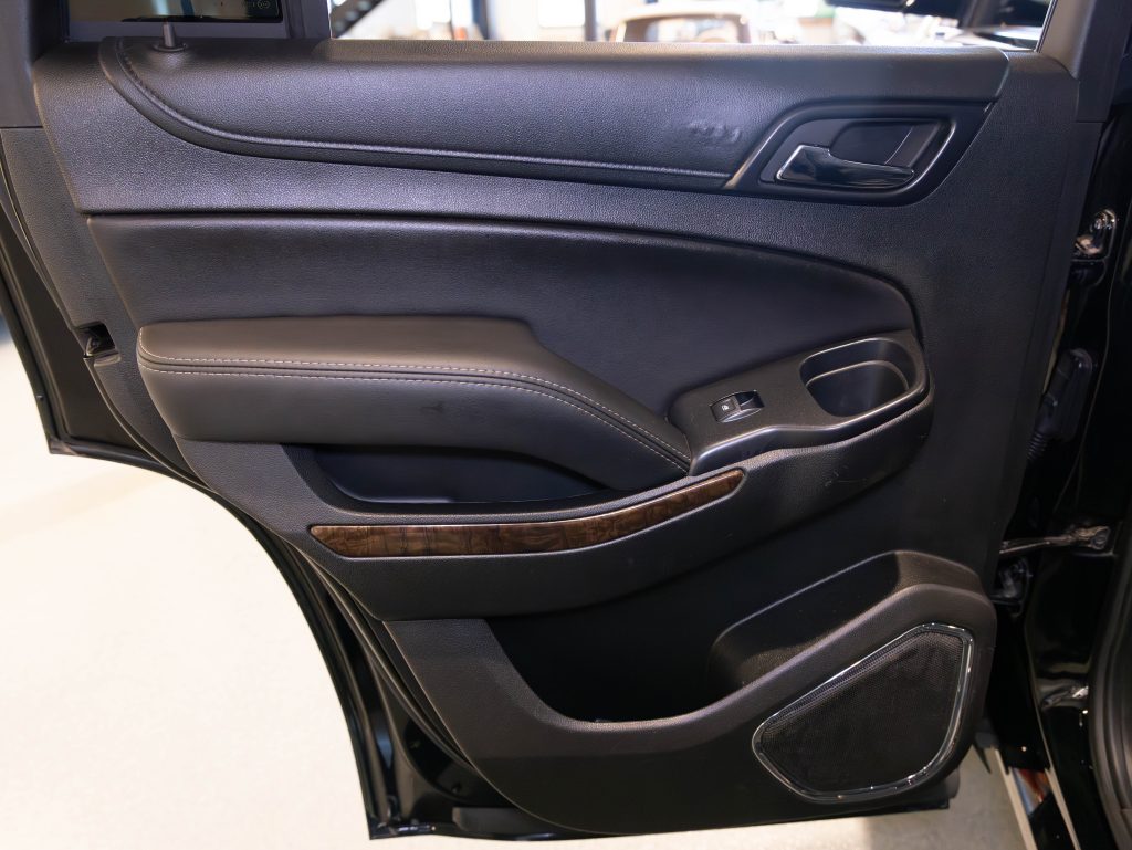 Interior view of a car door with a black finish, featuring a door handle, power window controls, storage compartment, and a speaker. - Monarch Showroom