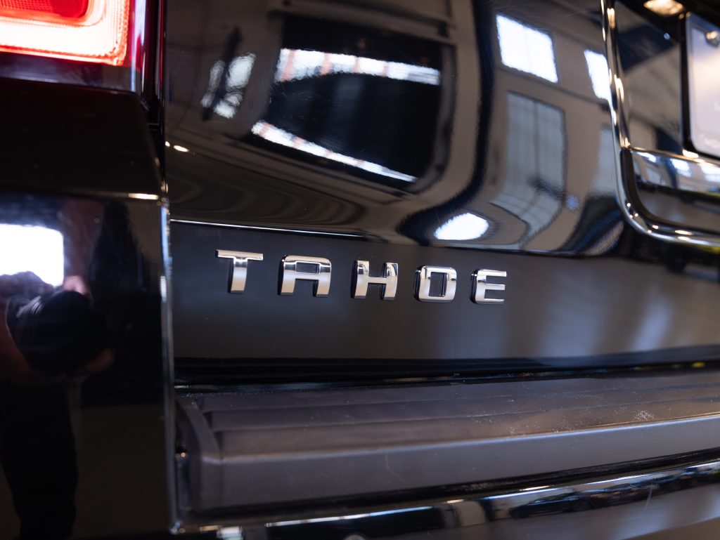 Close-up of the rear of a black SUV, displaying the silver "TAHOE" emblem on the back panel. - Monarch Showroom