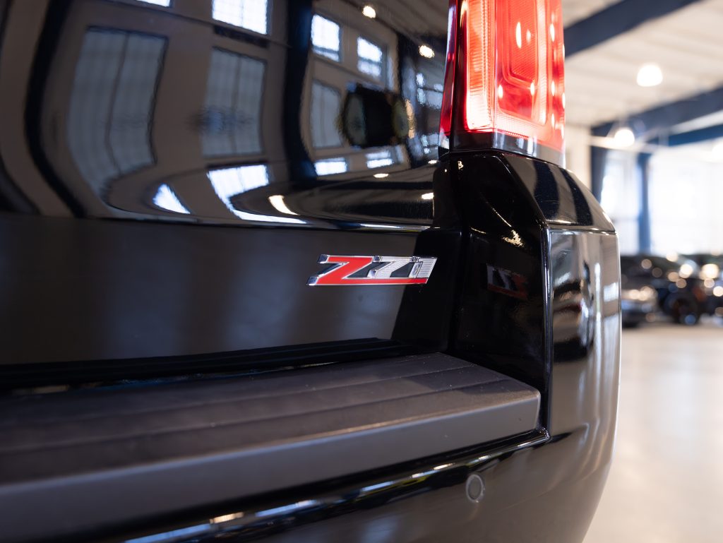 Close-up of a black vehicle's rear displaying a red and silver "Z71" emblem, with blurred interior of a garage in the background. - Monarch Showroom