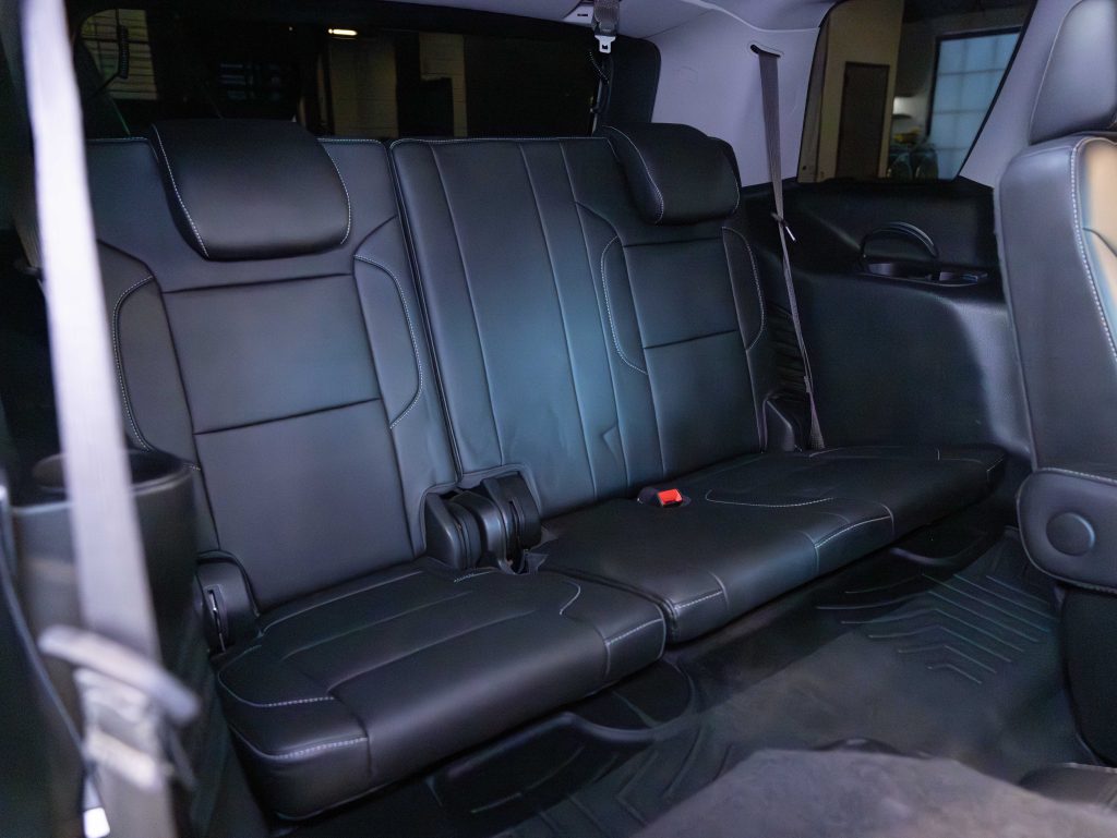 Interior view of a car's backseat featuring black leather upholstery with three headrests and a red seatbelt receptacle on the right side. - Monarch Showroom