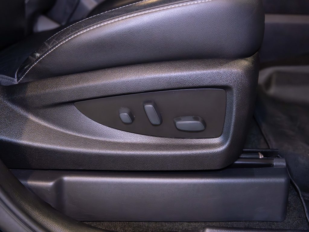 Close-up of a car seat adjustment panel with buttons for adjusting seat positions. The seat is upholstered in black leather. - Monarch Showroom