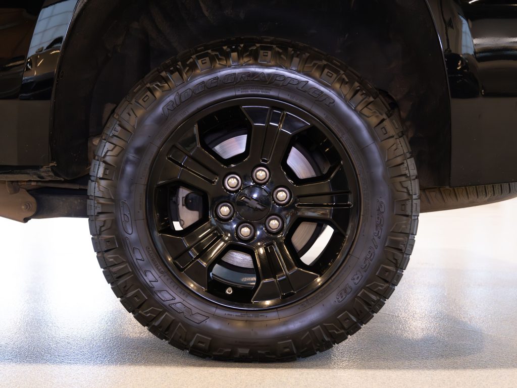 Close-up of a black truck tire with rugged tread pattern and five-spoke alloy wheel, fitted on a vehicle indoors. - Monarch Showroom