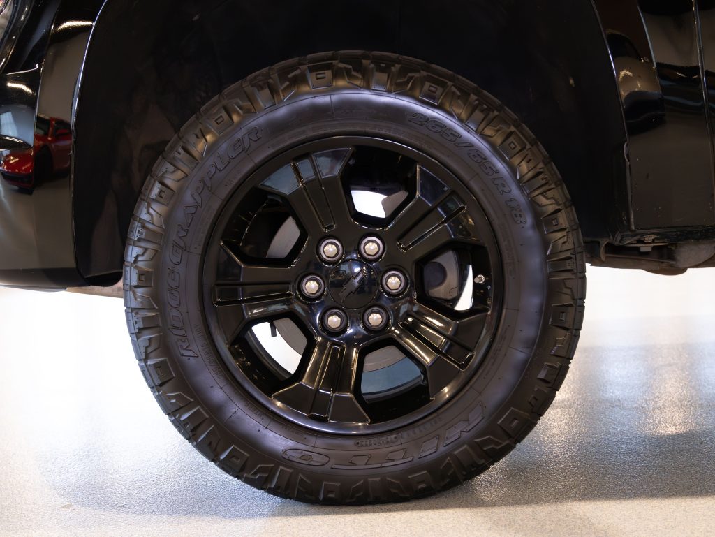 Close-up of a black vehicle tire with a five-spoke alloy wheel design on a light gray floor. - Monarch Showroom