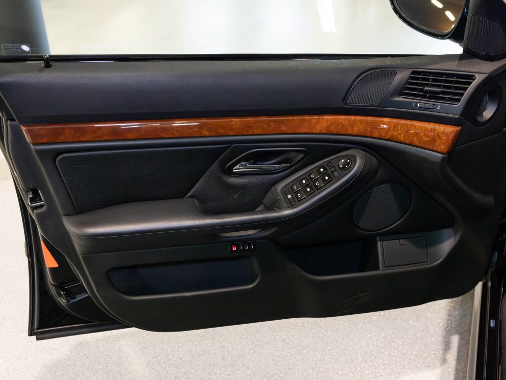 Car door interior with black and wood accents, featuring a handle, window buttons, and speaker. - Monarch Showroom