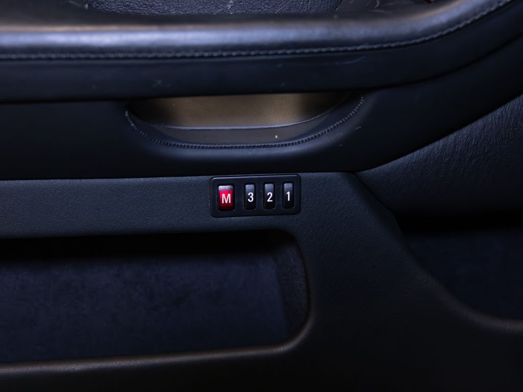Close-up of a car interior featuring black leather and four buttons labeled M, 3, 2, and 1 in a row. - Monarch Showroom