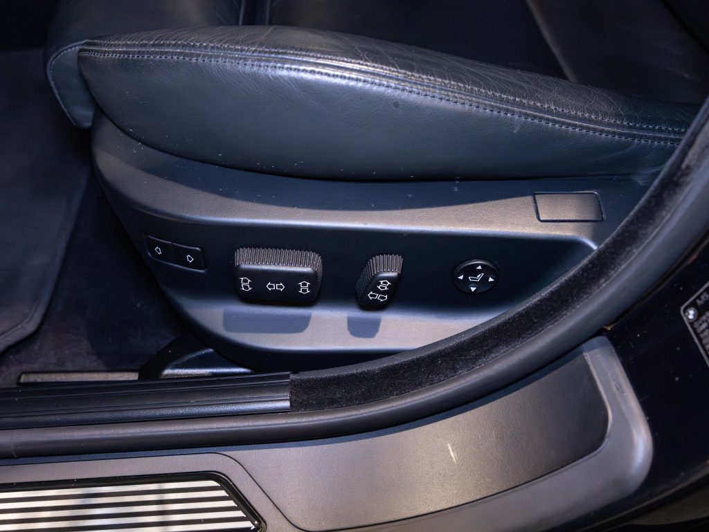 Close-up of car seat adjustment controls on the side of a black leather car seat, featuring buttons and dials for lumbar support and seat position customization. - Monarch Showroom